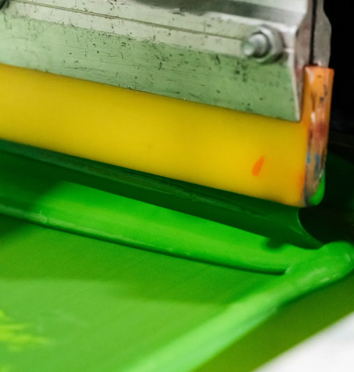 Nahaufnahme: Eine gelbe Rakel schiebt limettengrüne Druckfarbe über das Sieb.