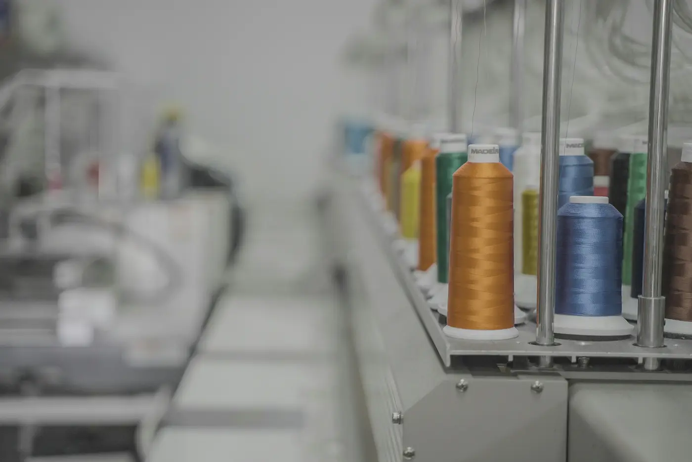 Garnkonen in Orange, Blau und Grün auf dem Garnständer einer Stickmaschine.